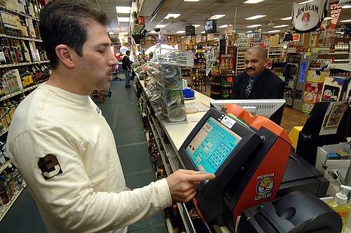 Nick Matti, owner of Bee Bee's Liquor Store in Warren, processes a ticket for customer Jose Vas on the store's new touch-screen lottery machine.